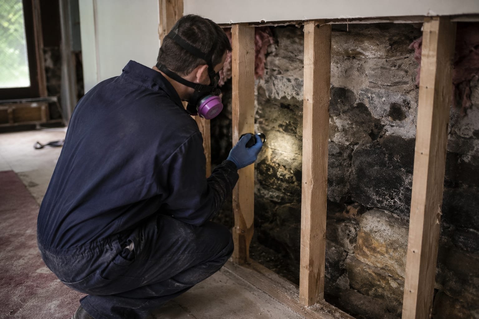 Mold remediation technician examining a stone foundation wall in a 1920s Brighton, NY basement